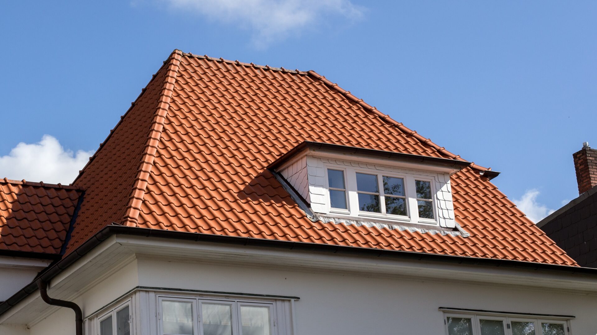 A white-sided home with orange tile roofing