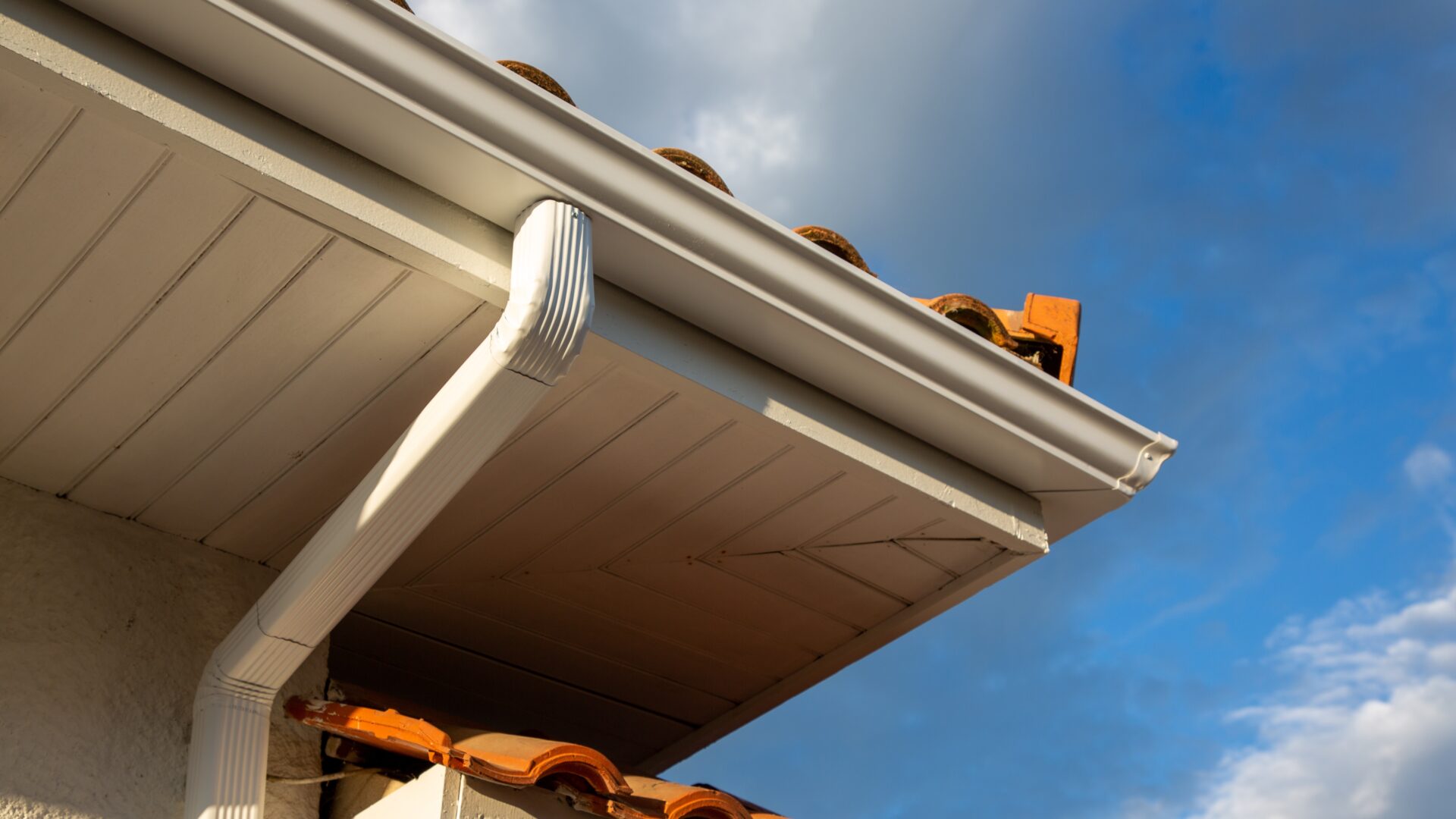 Closeup of a seamless gutter and downspout on a home with orange tile roofing