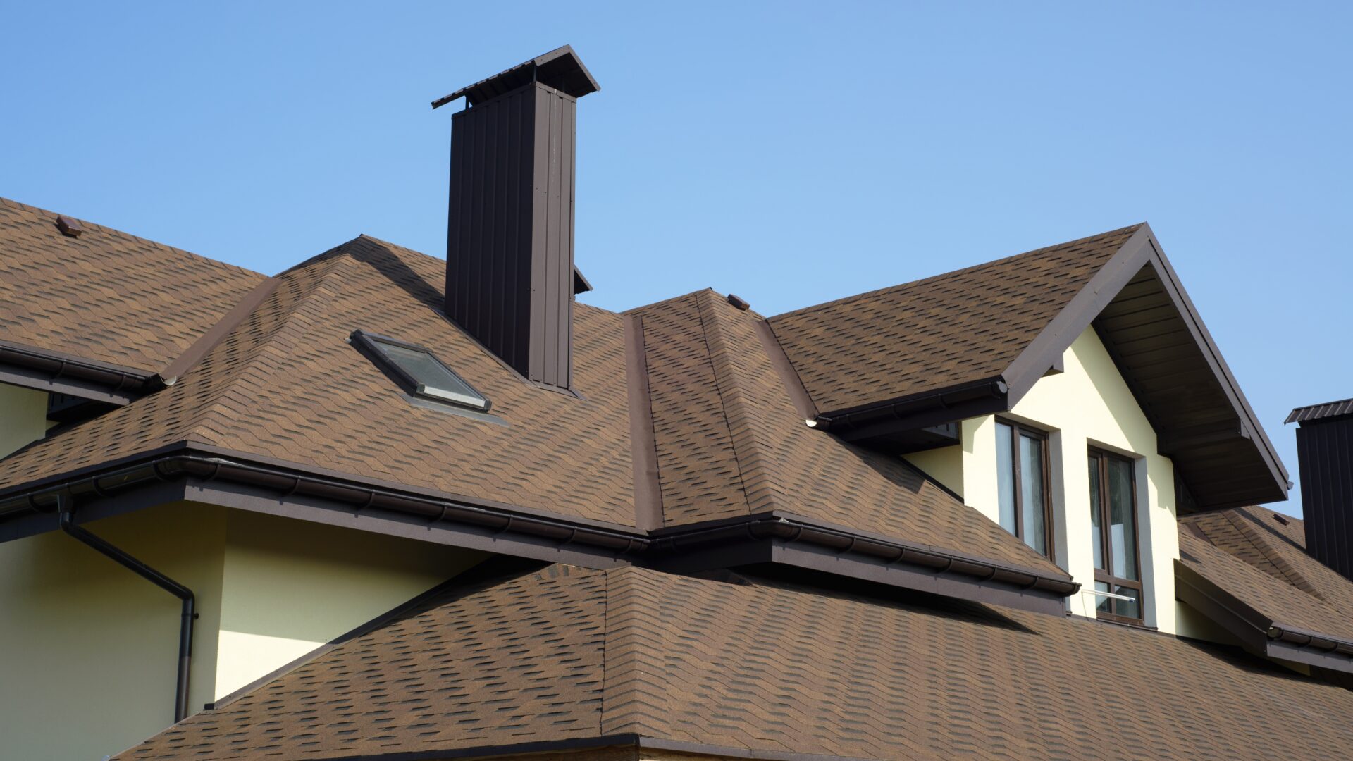 A brown shingle roof with a chimney on a cream-colored house